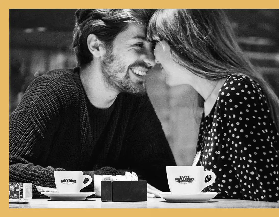 A man and woman sitting at a table with cups of coffee.